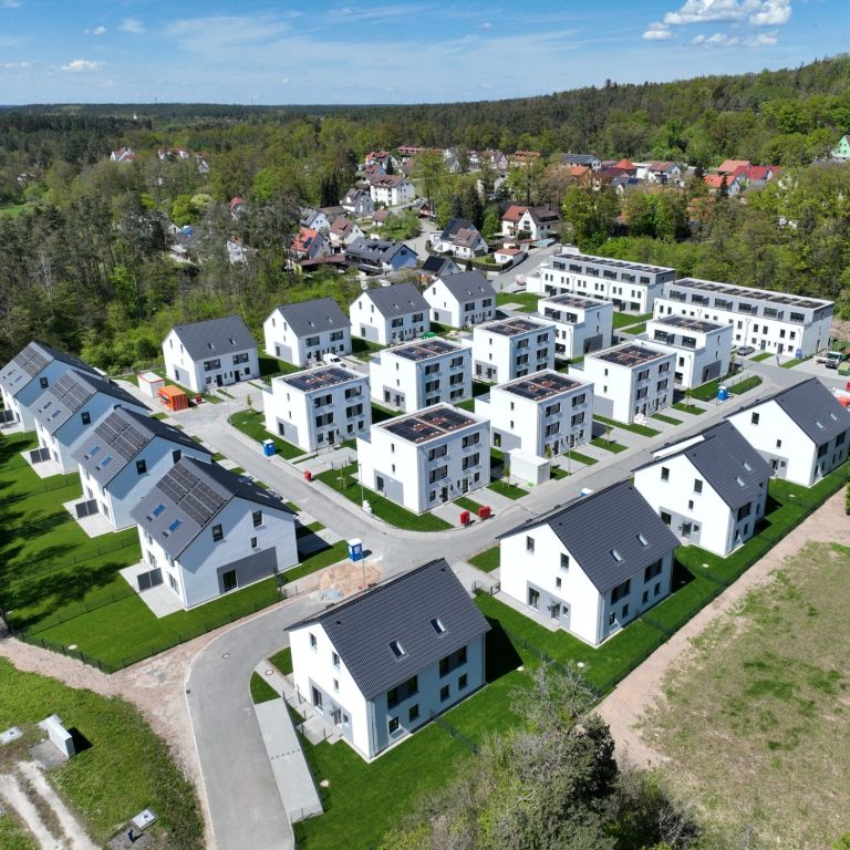 Immobilie Moderne Wohnsiedlung mit weißen Häusern und grünen Flächen, umgeben von Bäumen.