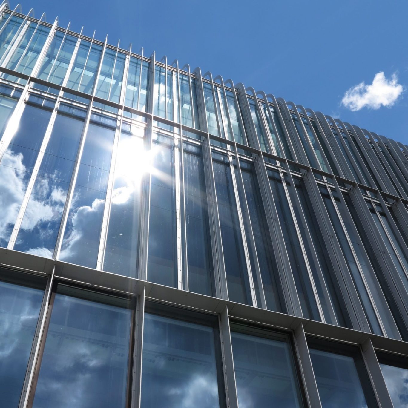 Glasfassade reinigen Moderne Glasfassade eines Gebäudes unter blauem Himmel mit Wolken.