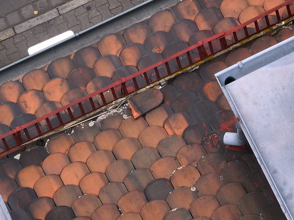 Sturmschaden Dach mit orangefarbenen Ziegeln und einer roten Leiter im Vordergrund.